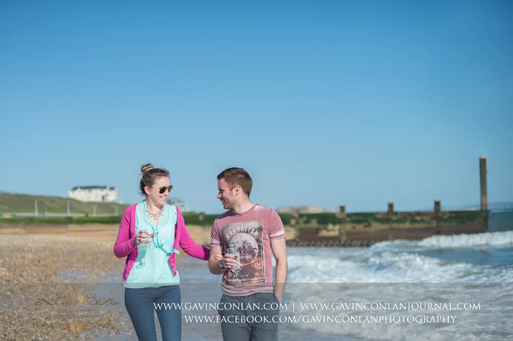 creative and fun portrait of Victoria and James walking along the beach near Boscombe Pier . Engagement Session in Bournemouth, Dorset by gavin conlan photography Ltd