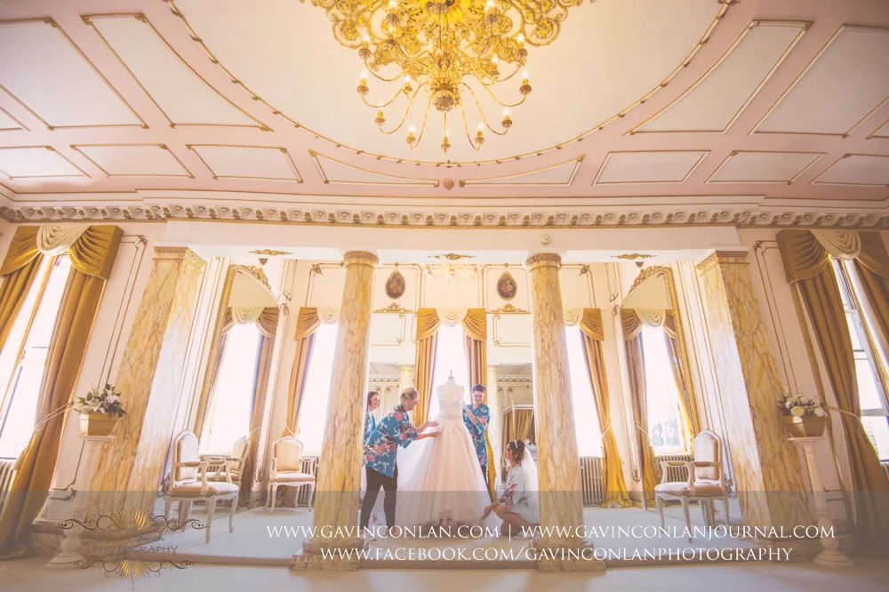 portrait of the bride and her bridesmaids looking at the brides wedding dress in The Rococco Suite. Wedding photography at Gosfield Hall by Essex wedding photographer gavin conlan photography Ltd