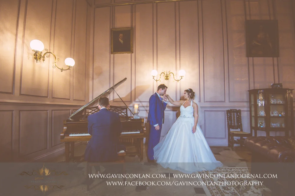creative and romantic portrait of the groom kissing his brides hand as the piano is being played. Wedding photography at Gosfield Hall by Essex wedding photographer gavin conlan photography Ltd