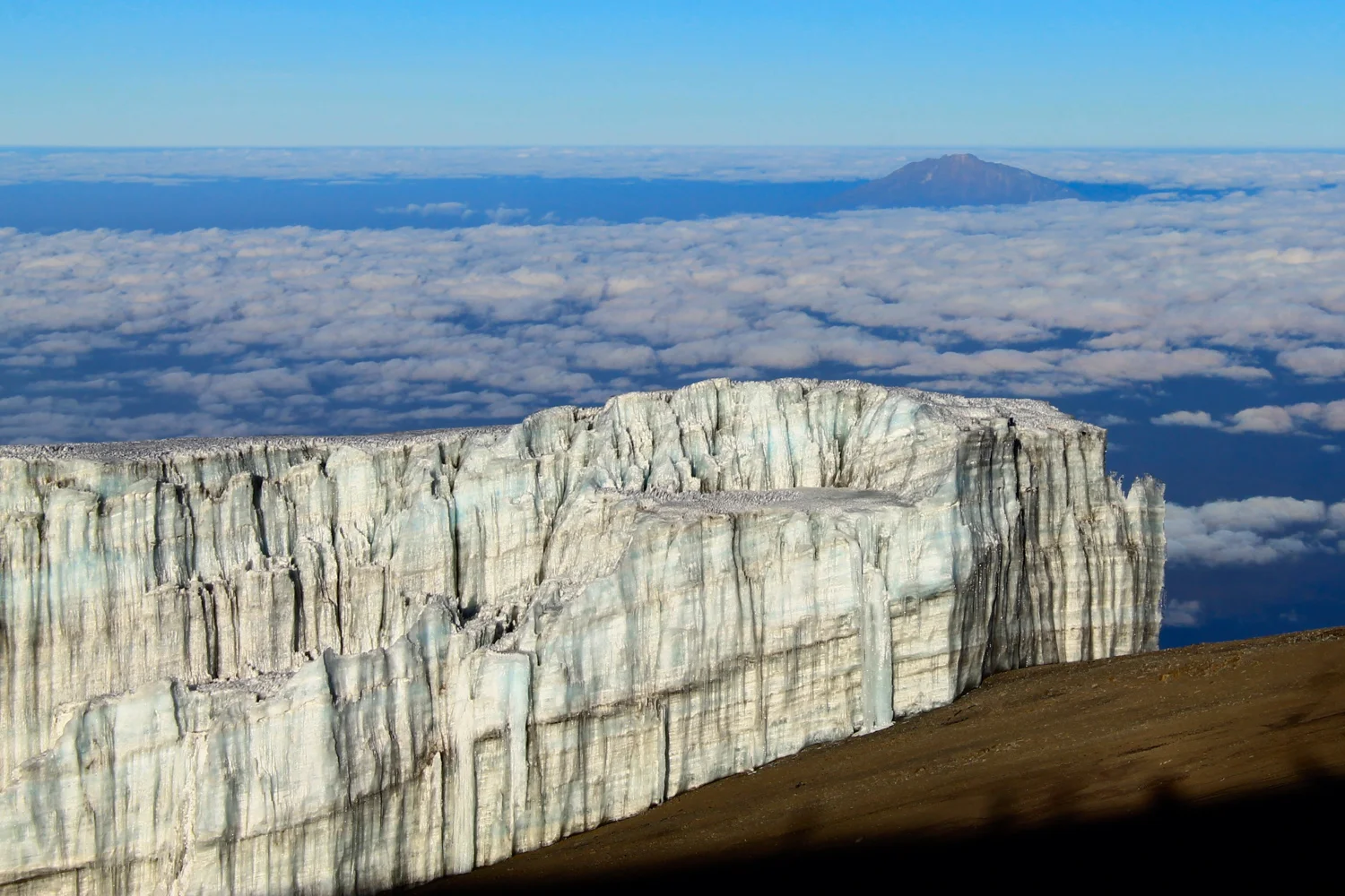 Glacier near the top of Mount Kilimanjaro with Mount Meru across the clouds.