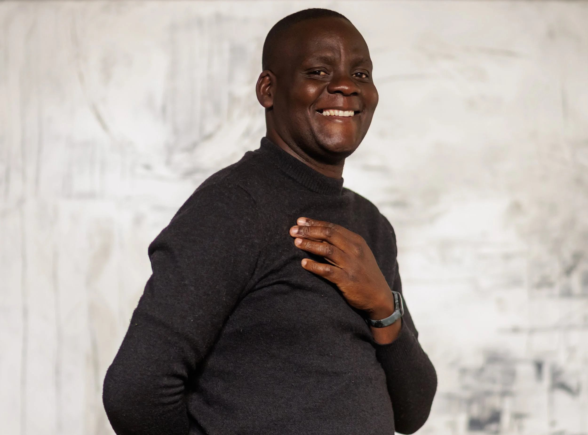 A smiling man with short hair wearing a dark, high-neck jumper and a wristwatch.