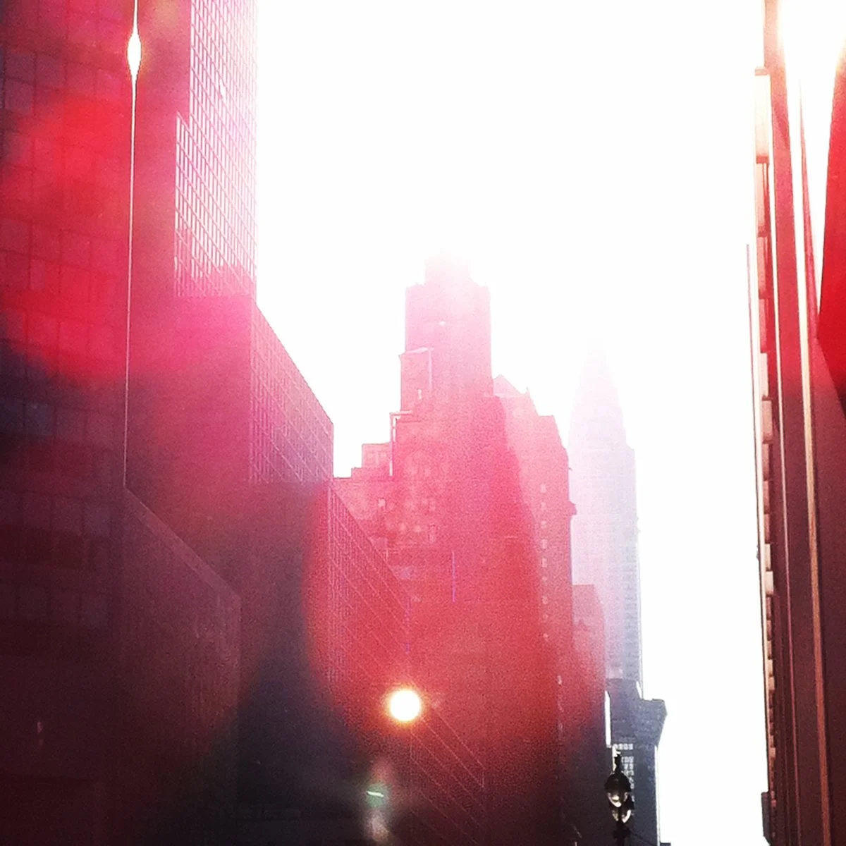 New York City skyscrapers with the sun reflecting off glass buildings, creating a bright and slightly pinkish hue in the scene.