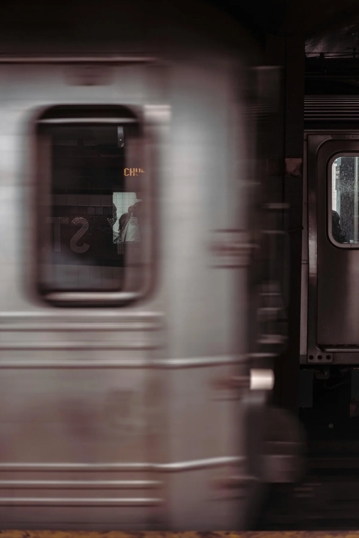 Moving NYC subway train with a blurred exterior and a reflection of a woman in the window.