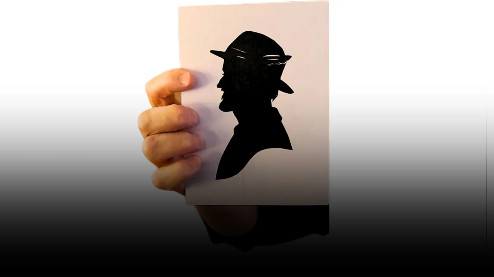 Hand holding a card featuring a black silhouette of a masked, hat-wearing man
