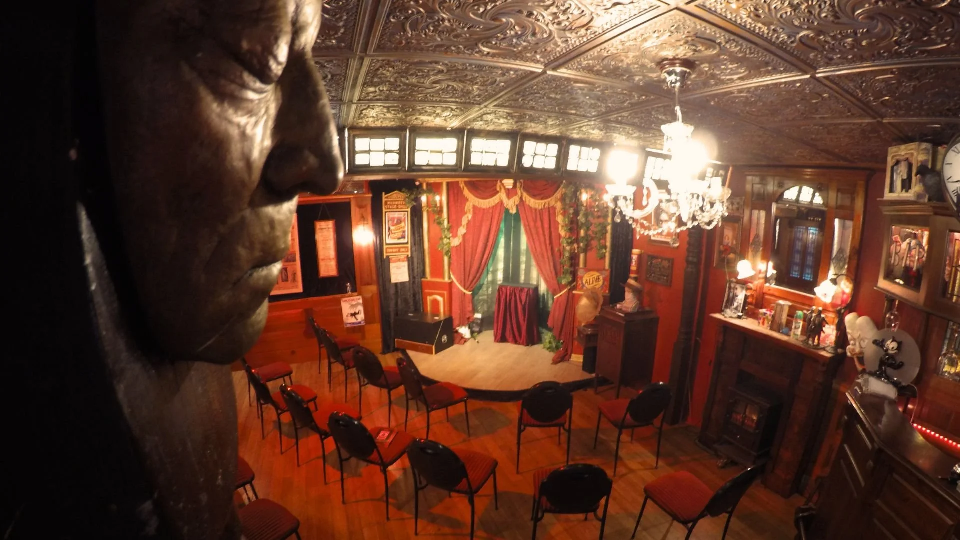 Ornate Victorian-style theater interior with red velvet curtains, chandelier, vintage decor, and rows of chairs