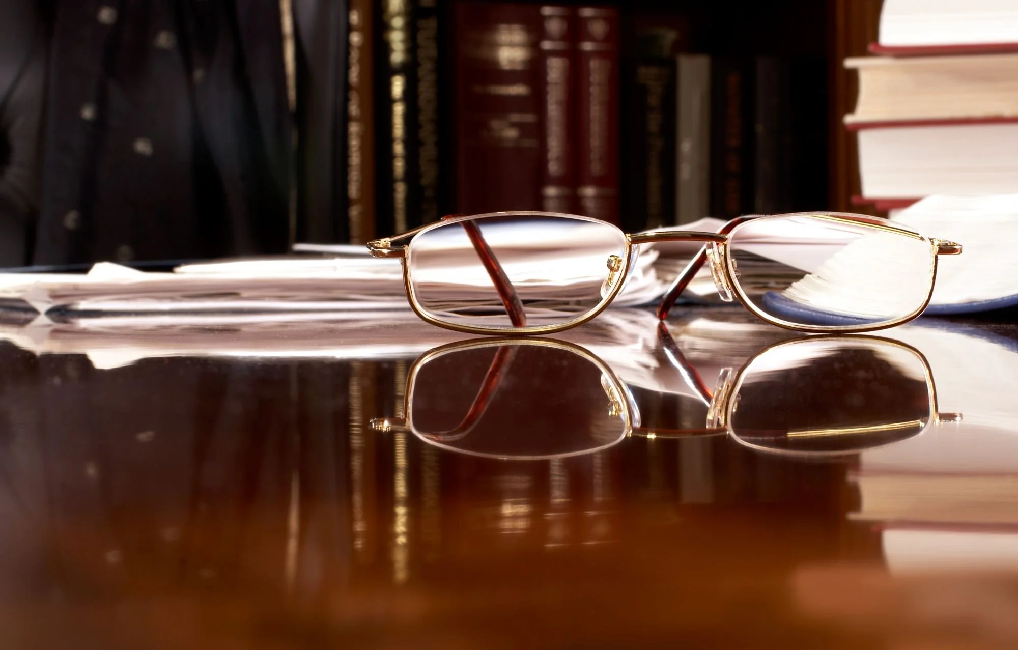 Eyeglasses resting on a desk beside books in a softly lit office.