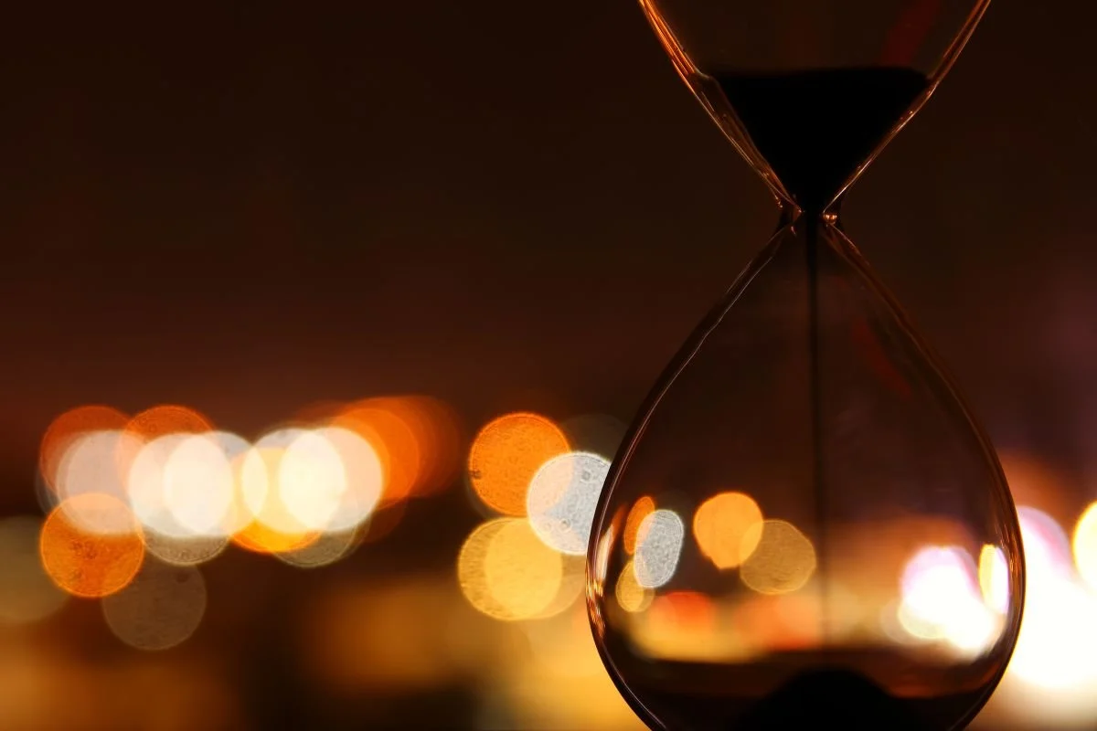 Hourglass against warm, out-of-focus lights, representing time-sensitive executive job-offer and counteroffer decisions.