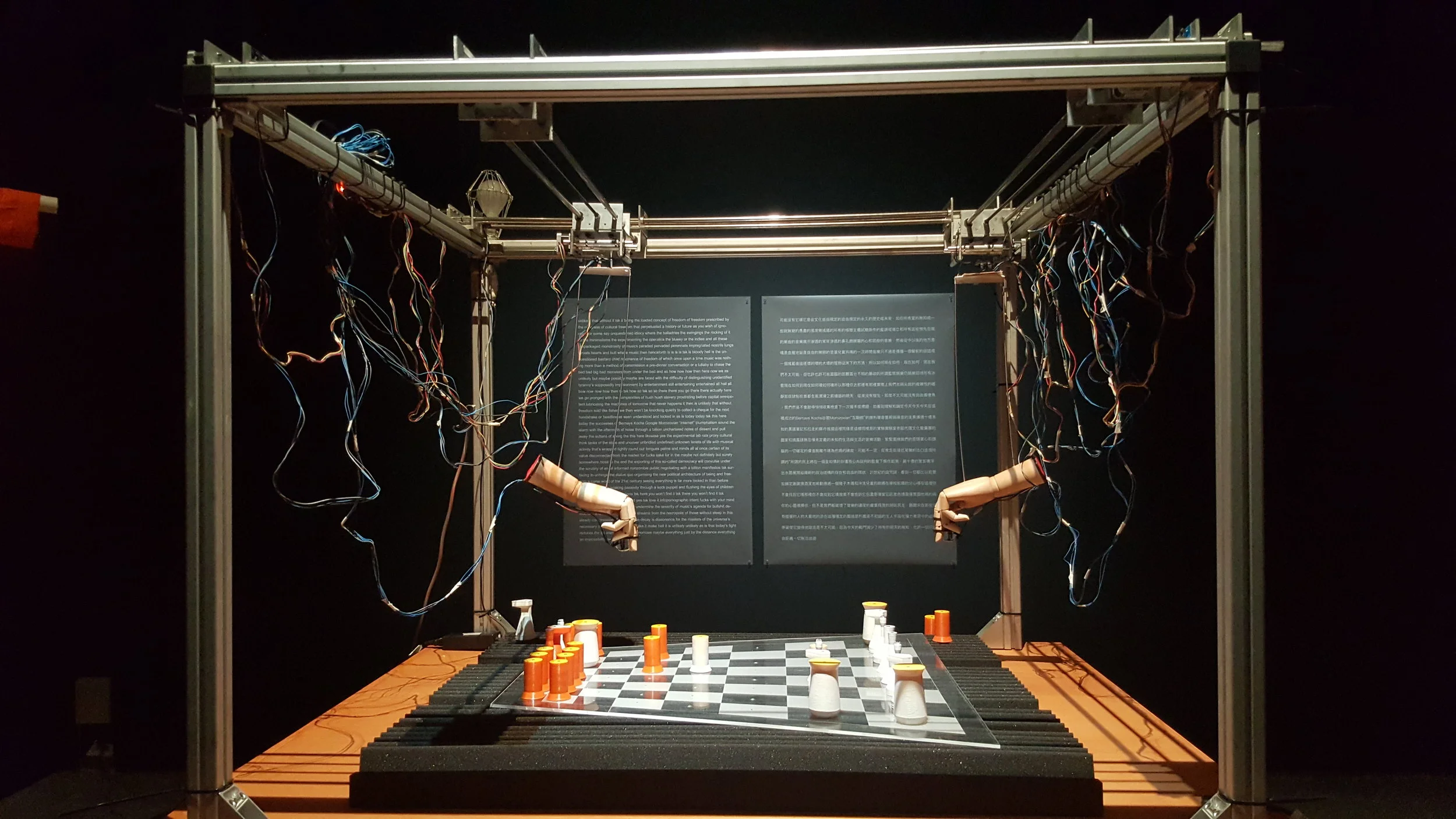 An out of the world, oddly-shaped chess game played between two wooden mannequin hands that are made alive by an explosion of wires dangling behind them.