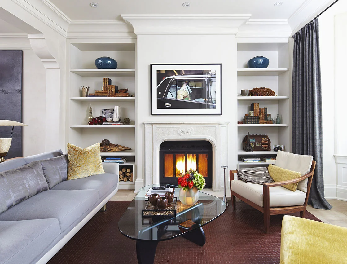 From the previous renovation, the only thing preserved was the original zero-clearance, wood burning fireplace. A custom designed mantle was hand-carved with solid stone and finished with a beaver motif. The openings in the cabinetry housing the firewood are made of durable Caesarstone, eliminating scuffing, while matching the painted finish of the surrounding cabinets. The custom designed sofa provides seating around an original Noguchi coffee table. Family heirlooms and treasured accessories add a personal touch.