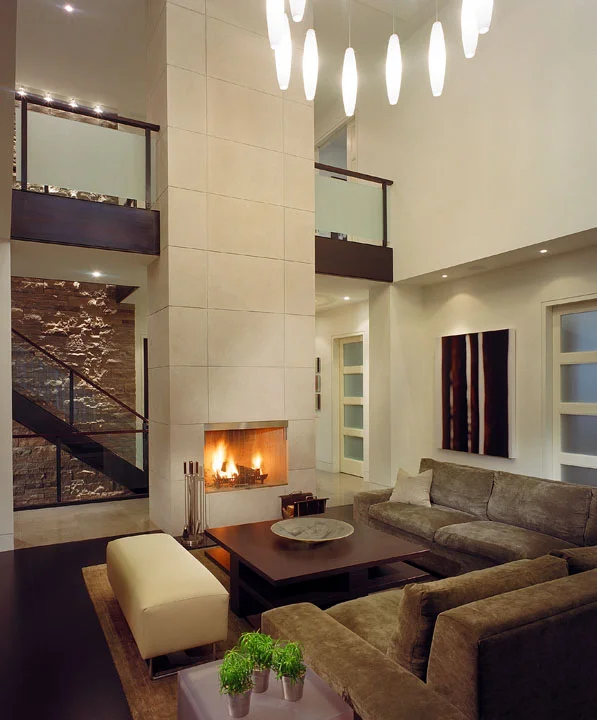 Designed to provide the perfect backdrop for a growing modern art collection, the orderly living room of this new family home is simply furnished with both classic pieces and unique custom-designed items. In its 2-storey great room, a stunning fireplace wall emphasizes the floating stair and 3-storey stone wall at the home’s core. A custom light fills the open volume.