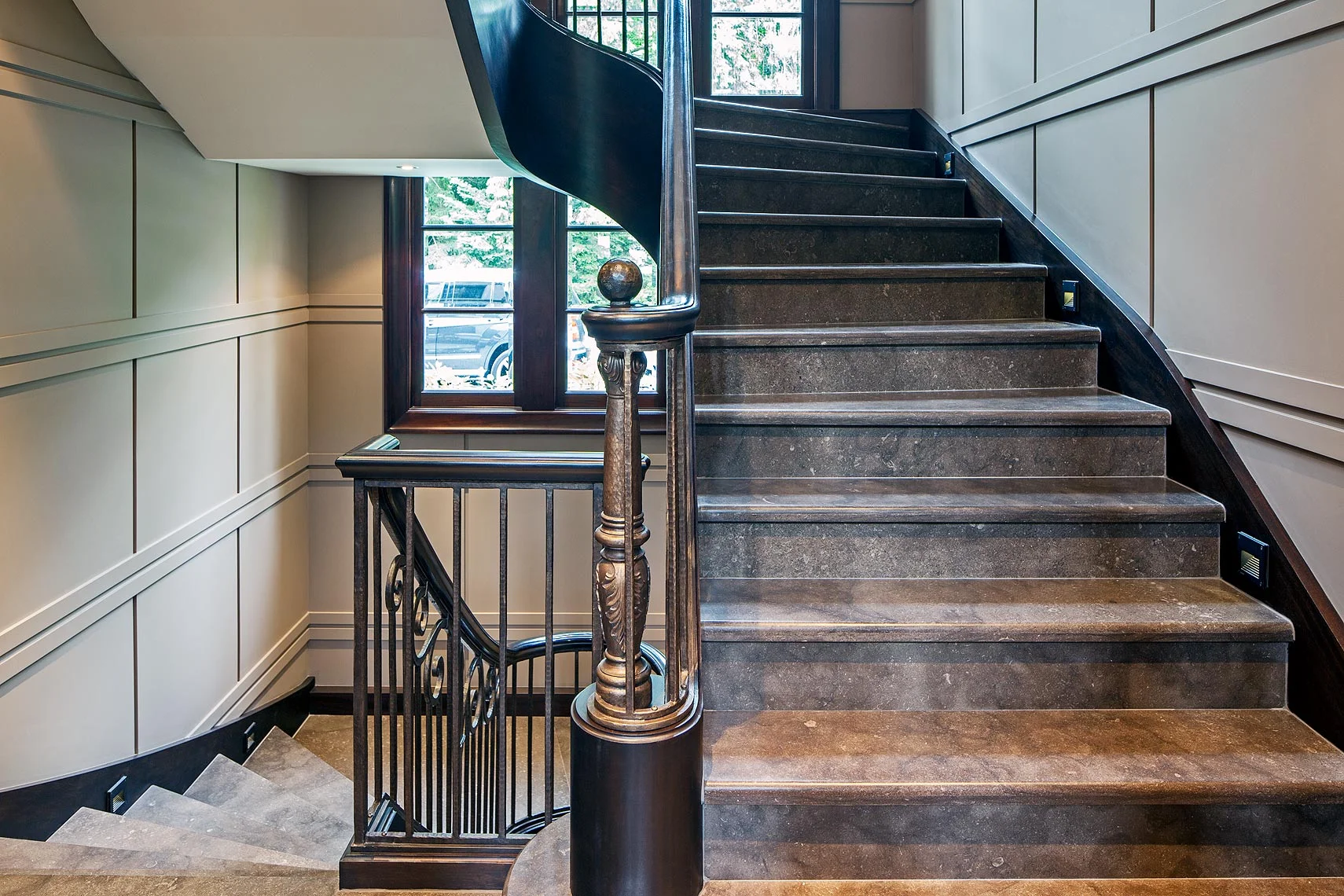 Texture is a key design element in this stately home, as seen in the double-rail-and-reveal detail of the contemporary painted wooden wall panelling, the wooden cladding on the steel stair structure into which stone steps have been set and the contemporary bronzed iron railing.