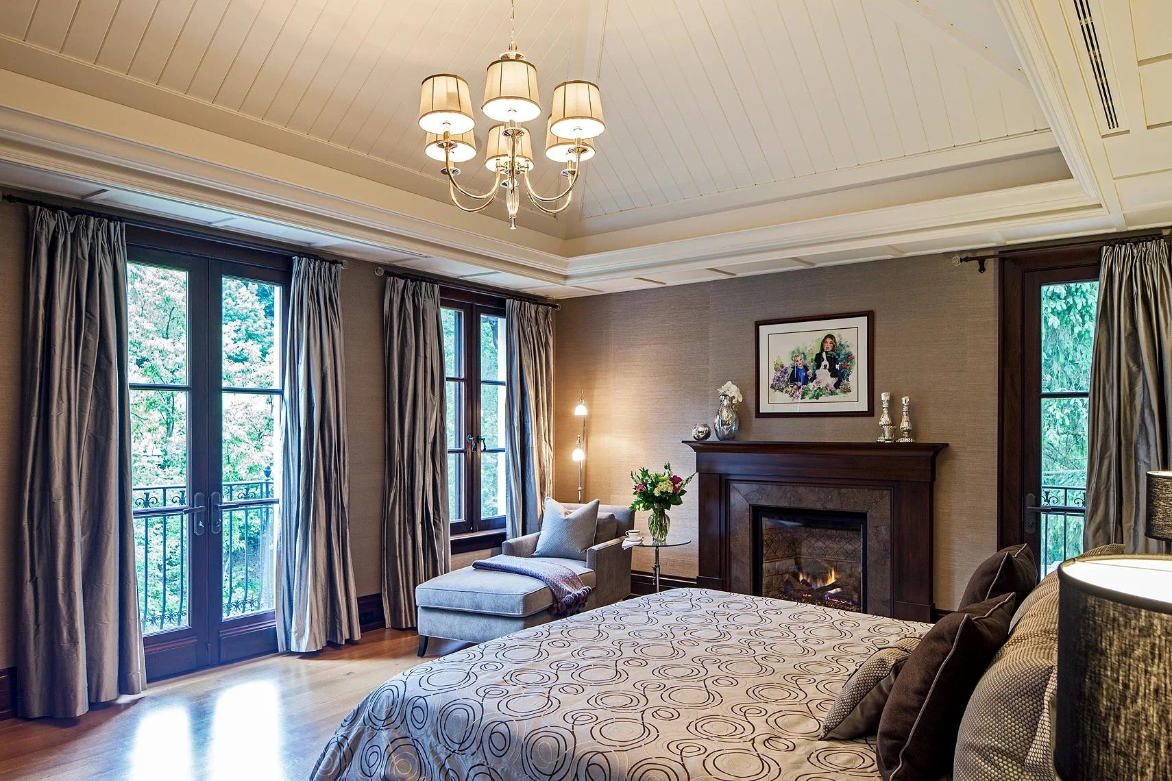 Cleverly integrating ventilation ducts, the painted wood panelled ceiling emphasizes the gracious expansiveness of this tranquil room. Extra-full pale silk drapery flanks the large mahogany framed windows overlooking the forest landscape. Mahogany also completes the St-Marc-des-Carrieres limestone in the custom fireplace surround. The walls are covered in pale grey grass cloth.