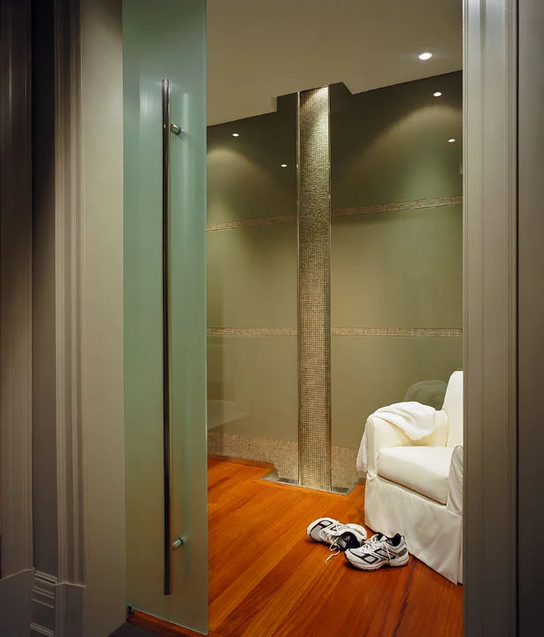 This lower level spa is introduced by a narrow, spot-lit crevasse waterfall slot. We asked the architect to lower the waterfall space by two feet to allow for under-floor services. The centre panel of teak flooring lifts out for easy access to pump, plumbing and electrical. We also dropped the ceiling in this area for proportion and to hide the angle of the stairs above.