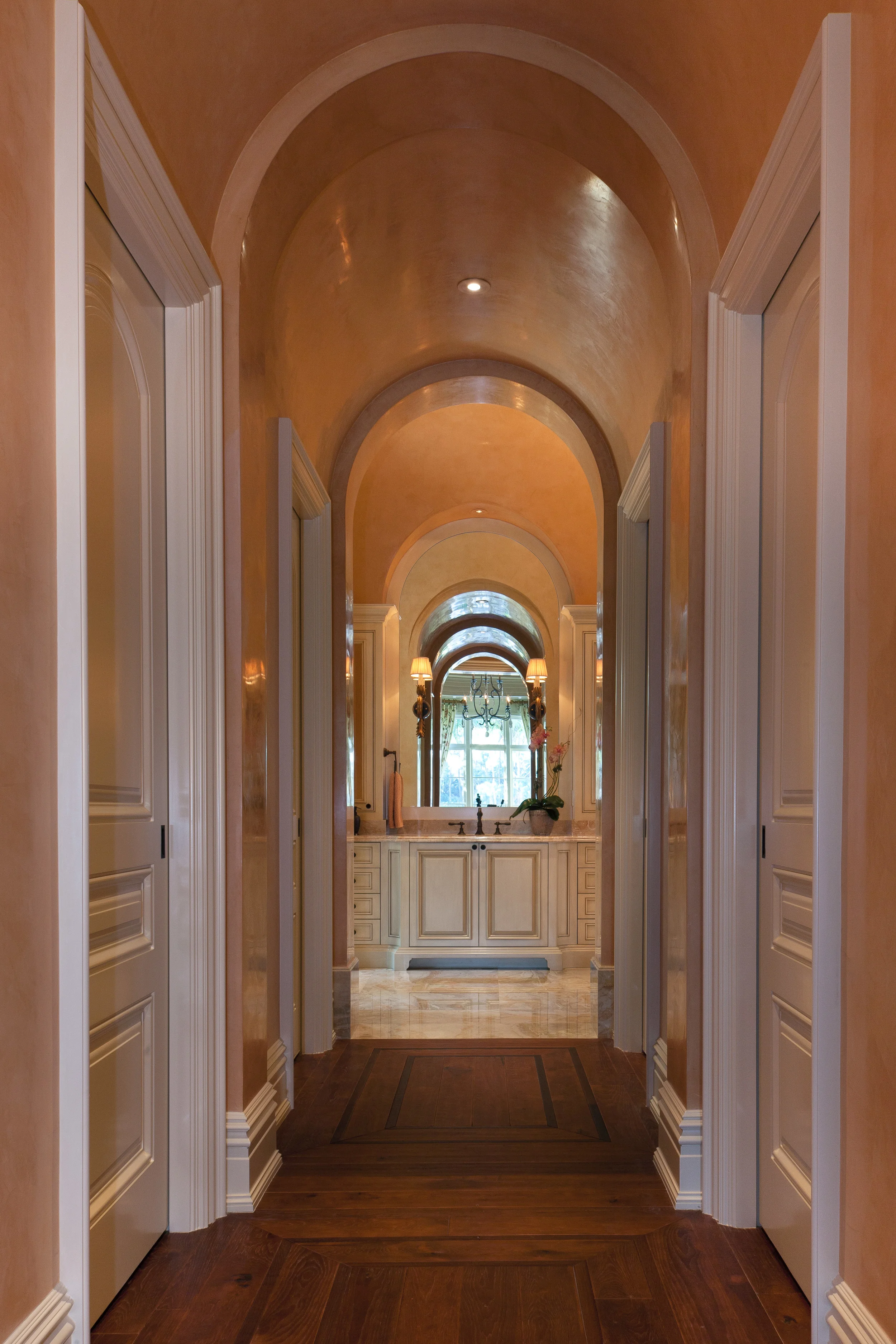 Seen from the master bedroom doorway, this short corridor leads to the master bath and incorporates openings to dressing rooms, toilet area and shower room on either side. The delicate archway and fine plaster finish reflect the other finishes in the home; the hickory flooring is used throughout, in diverse patterns. The gracefully detailed vanity cabinetry at the end of the corridor rises above breccia oniciata marble slab flooring.