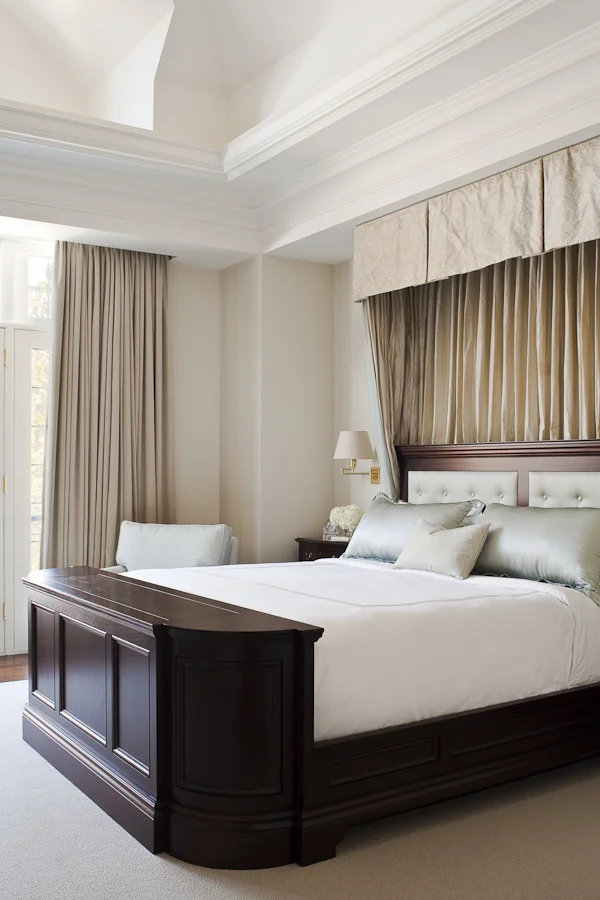 We worked with the builder of this very traditional home to resolve and sculpt the vaulting for this large room, adding a false interior slope to match an existing corner and creating a bulkhead across the window to join them. Below a silk damask half-canopy, the large custom bed was detailed with a graceful curved corner to minimize its visual bulk and with an ingenious pop-up television screen.