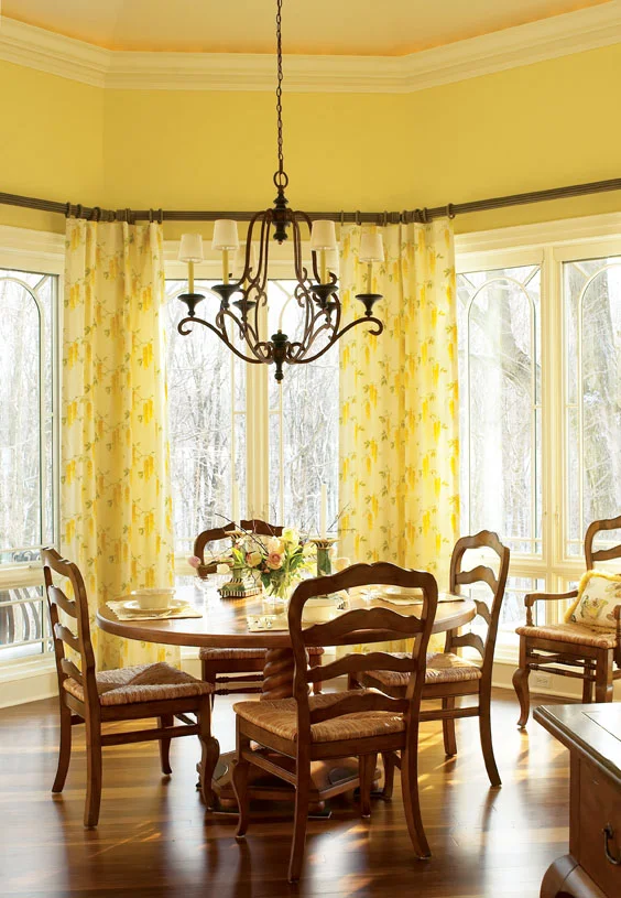 In the family farmhouse kitchen, a large bay window floods the room with light and provides a woodland view. We used a sunny yellow palette and cheerful semi-sheer draperies to welcome and amplify the breakfast sunlight.