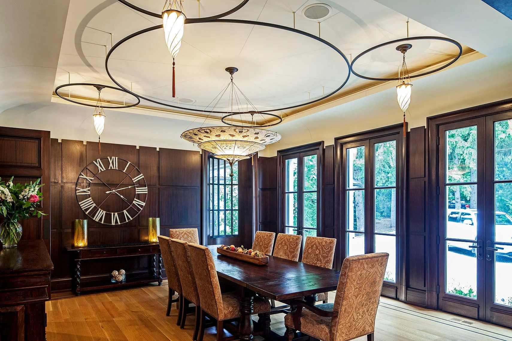 The formal dining room’s simple elegance is deceptive; founded as it is on layer upon layer of unusual details. Matching a wall alcove opposite, the D-shaped window on the end wall comprises thermopane lights in an iron frame. The reveal line around the recessed centre panel emphasizes the gentle curve of the sculptural transition to the oval ceiling. In the mahogany wall panels, recessed fixtures in the shortened reveals accentuate the resulting crenellation, while washing the ceiling curve with light. Above, floating iron rings frame the Fortuny silk pendant lamps.