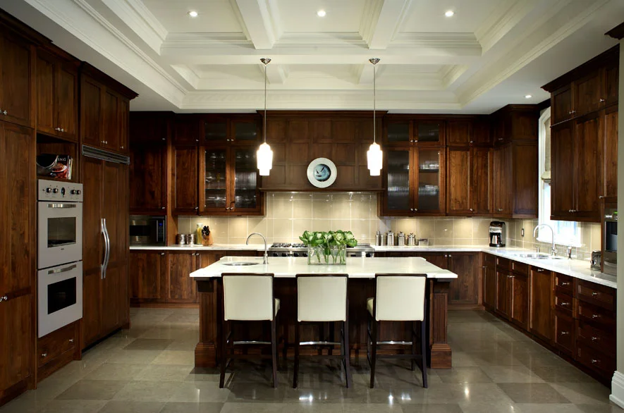 The generous kitchen’s traditional styling in the deeply coffered ceiling and elegantly detailed walnut cabinetry contrasts with gleaming glass tile and stone surfaces and contemporary seating.