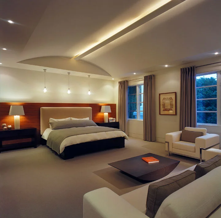 This serene and orderly master bedroom is finely detailed. The coffee table reflects the ceiling arch; the ceiling slot houses continuous strip uplighting; the headwall and nightstand units conceal lighting, A/V and security controls.