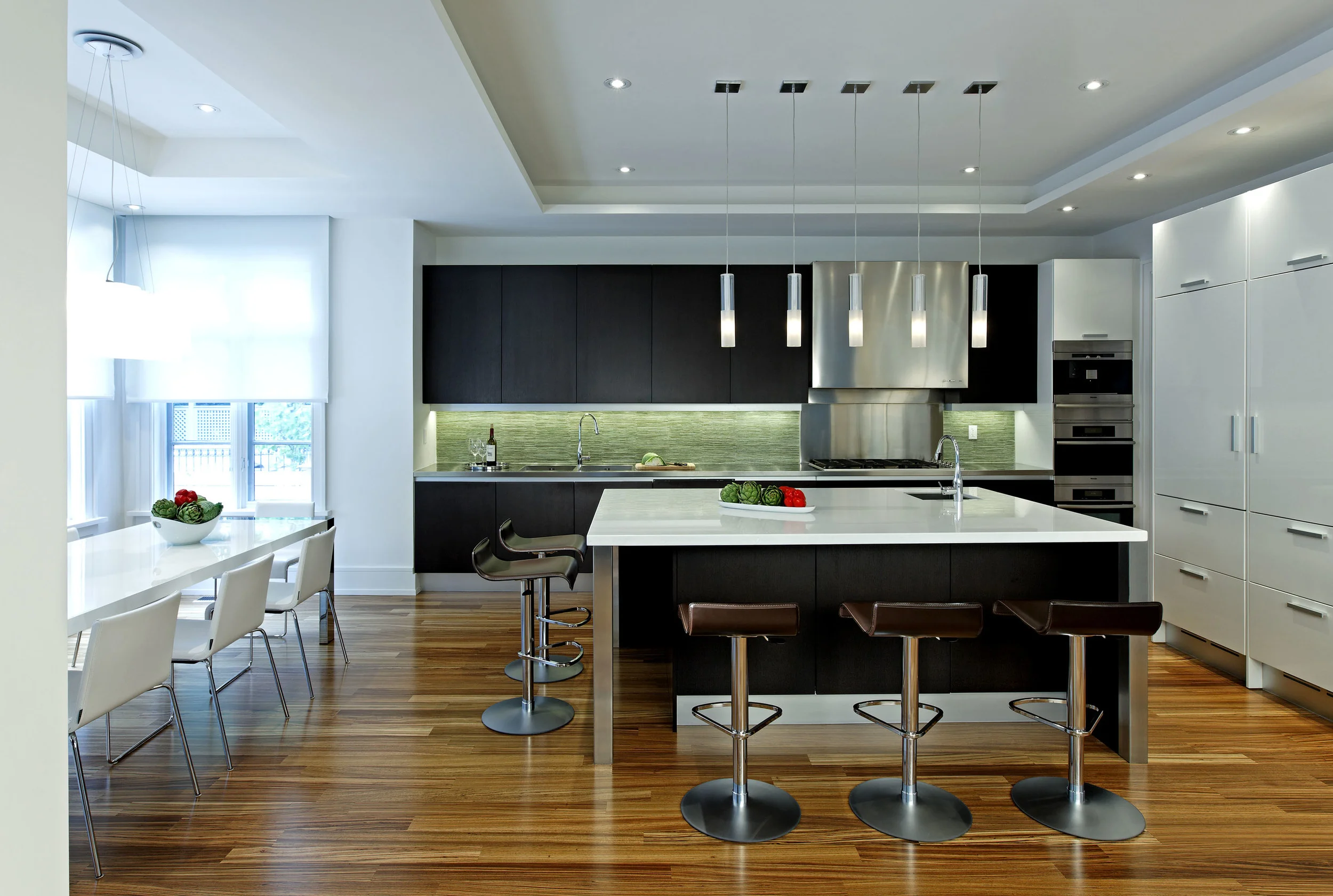 In the generous, light-filled kitchen’s asymmetrical layout, the sink, cook top and ovens align on a single dark wall; the storage / refrigeration on a white one. The whole family can gather at the large, square island.