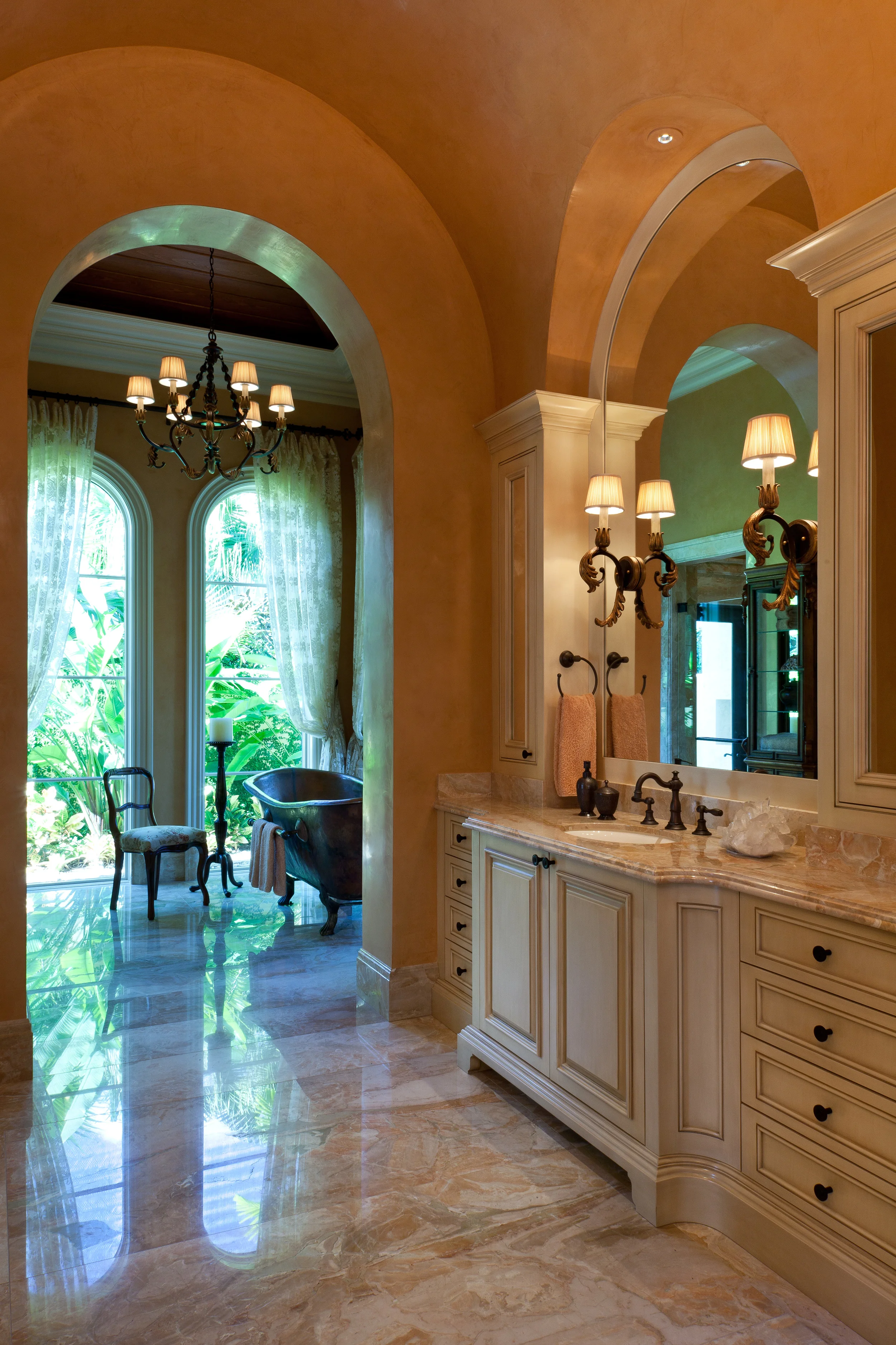 As in the other rooms in this exquisite Florida home, the architectural and cabinetry details were painstakingly developed to contribute to the interior design character individually and to work together beautifully. Here, the circles of the vanity mirrors reference the barrel vaulting of the ceiling and all the cabinetry was designed to enhance the volume. Venetian plaster, painted millwork and bronze fittings work well with the magnificent breccias oniciata marble slab flooring.