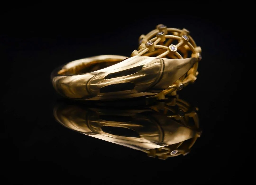 Gold jewelry bracelet with embedded gemstones, displayed on a reflective black surface.