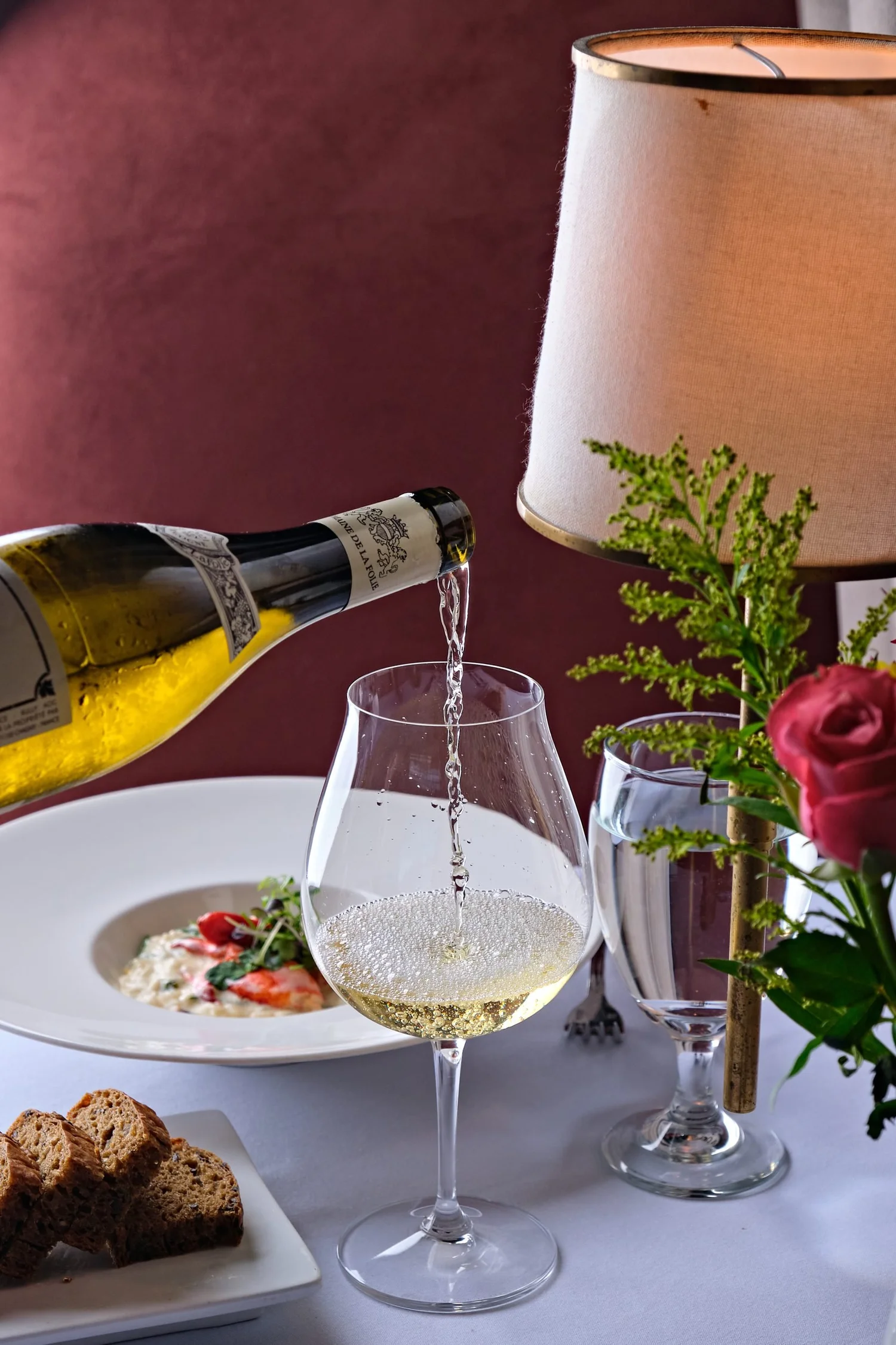 White wine poured tableside beside lobster risotto at The Black Pearl fine dining restaurant in Dunedin