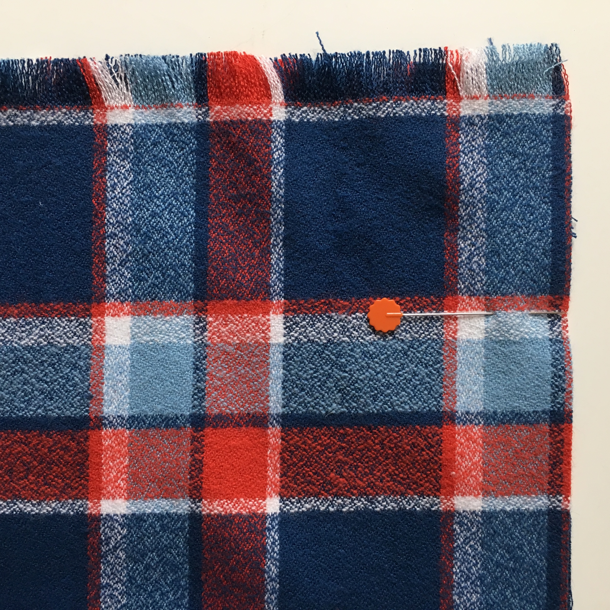 The scarf is folded in half the long way and pinned on the raw edge, matching the plaid carefully
