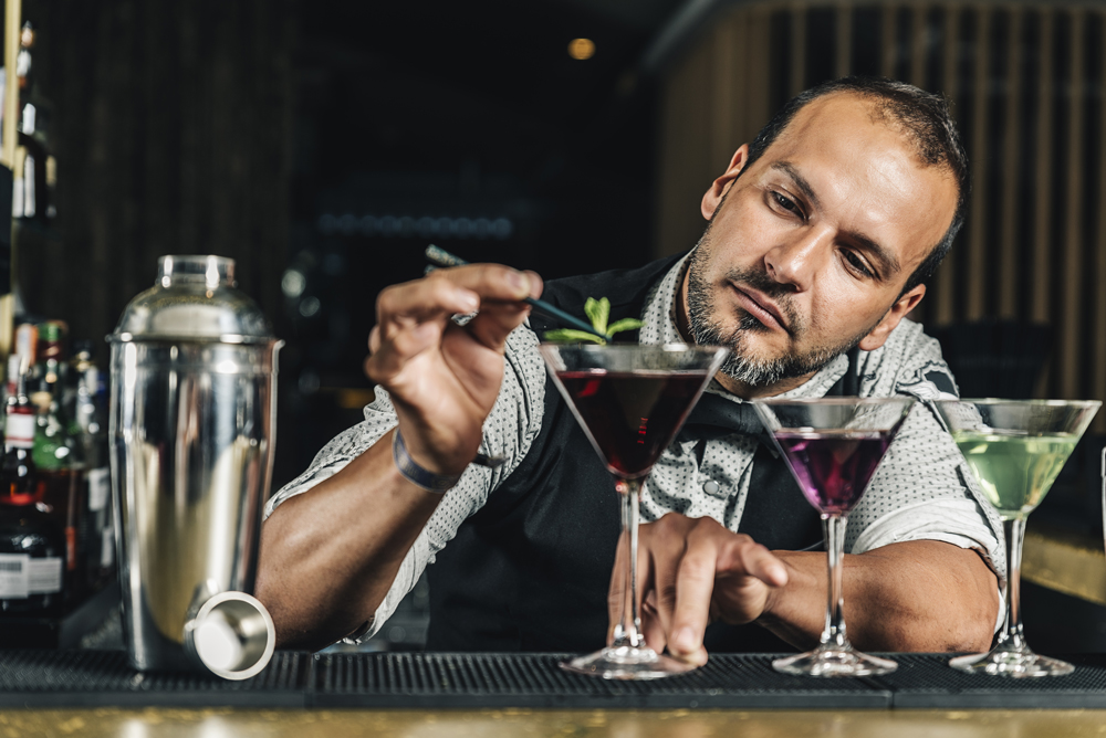 Victorian Bath House interior, barman garnishing a dark red cocktail in a tall-stemmed, conical glass