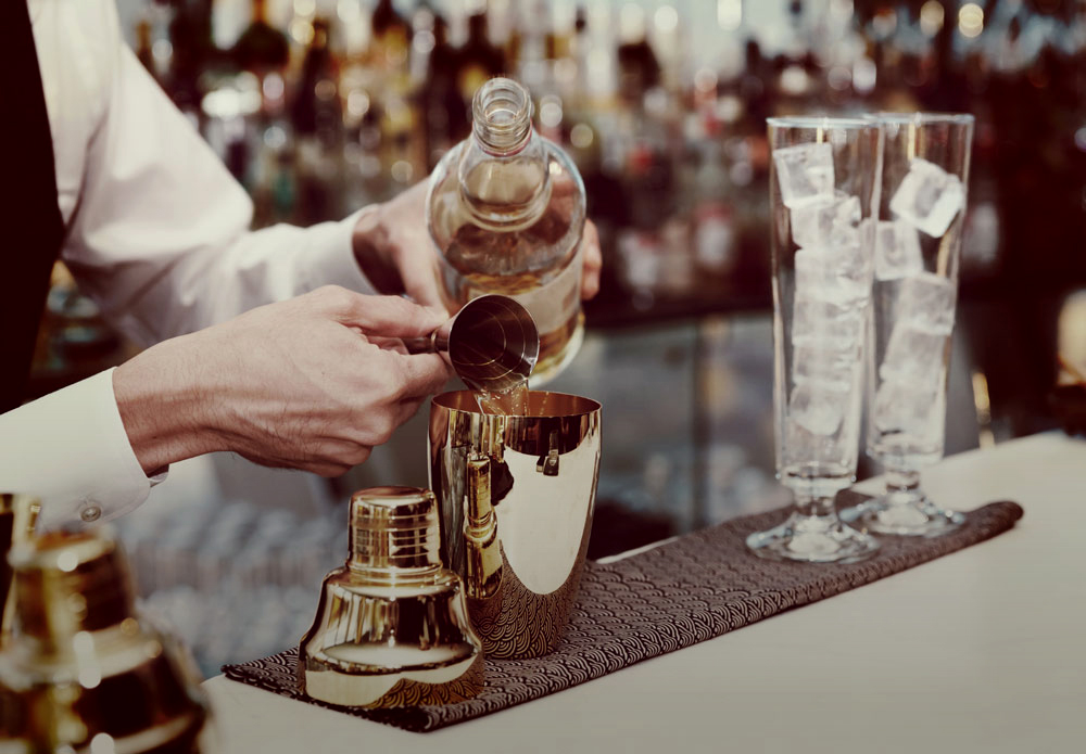 Victorian Bath House interior, barman pouring a measure of spirits into a cocktail shaker