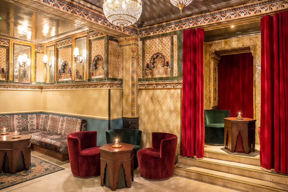 Victorian Bath House interior, richly patterned walls, curtains and furniture with chandeliers hanging from an ornate ceiling