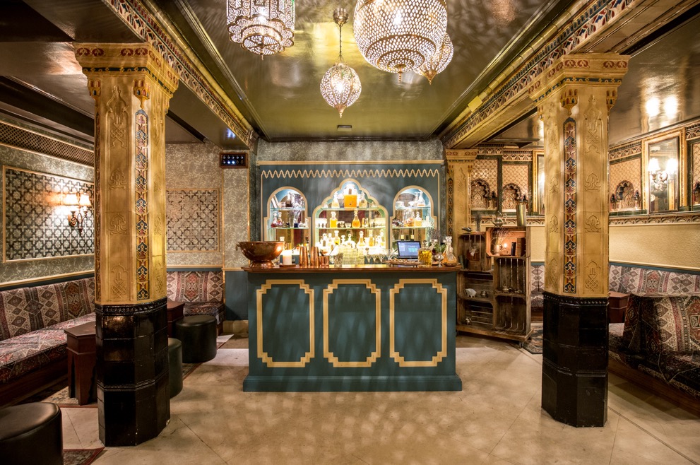 Victorian Bath House interior, richly patterned walls and furniture with chandeliers hanging from an ornate ceiling