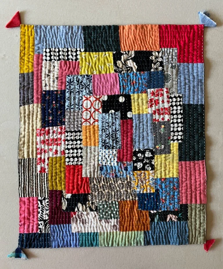 A colorful patchwork quilt with various patterned fabric squares, edged with fabric corner protectors in red and blue.