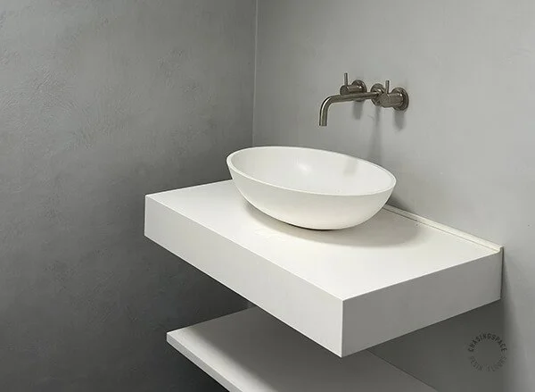 Minimalist white sink contrasting with seamless grey microcement surfaces.