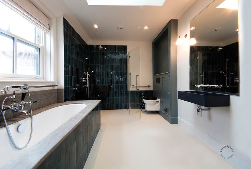 Modern bathroom with a skylight, featuring dark tiled walls and elegant fixtures. The sleek design is enhanced by a greige colour resin floor for a contemporary finish.