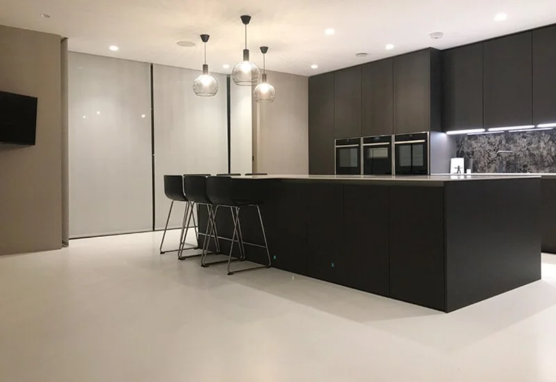 A modern kitchen featuring a sleek, seamless neutral resin floor and a large dark island with matching stools.