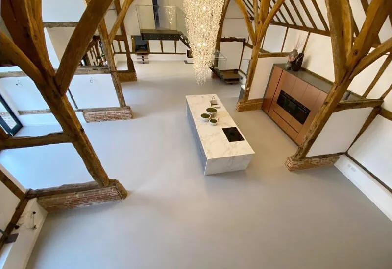 High-angle view of a grey resin floor in a kitchen area with exposed historic ceiling timbers.