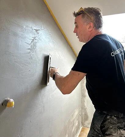 Hand smoothing a light-toned, polished microcement finish indoors.