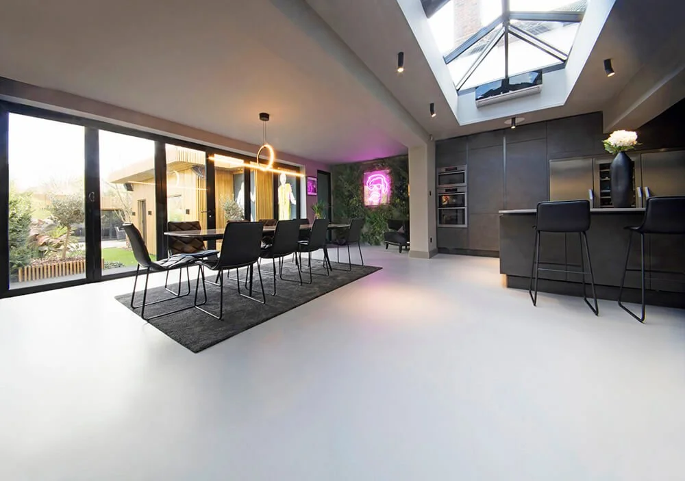Modern dining and kitchen area with large windows, skylight, black chairs, and a dark grey kitchen island.