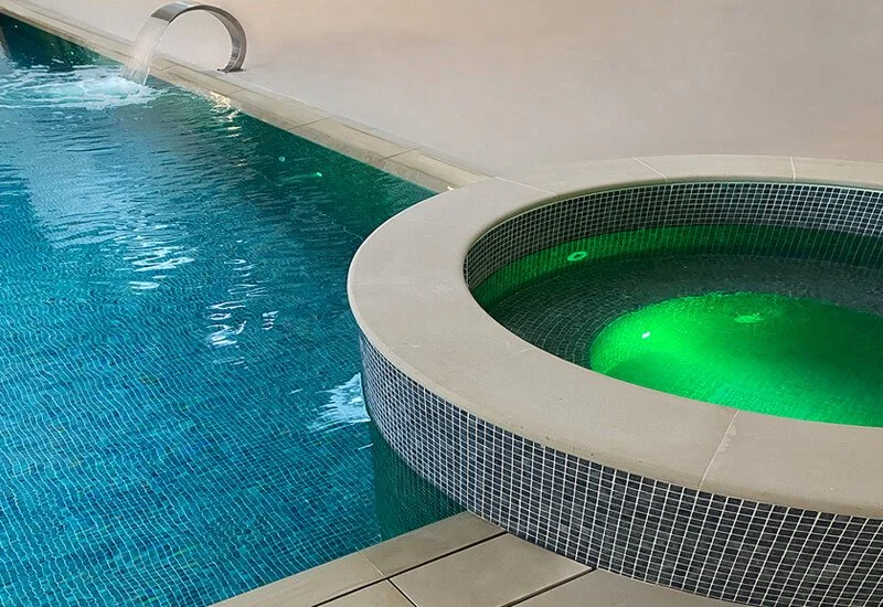 An indoor swimming pool and illuminated jacuzzi set against a smooth, modern resin floor in rib beige colour.