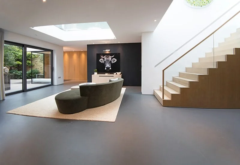 Modern open-plan interior with a dark resin floor highlighted by a feature wall and glass-railed wooden staircase.