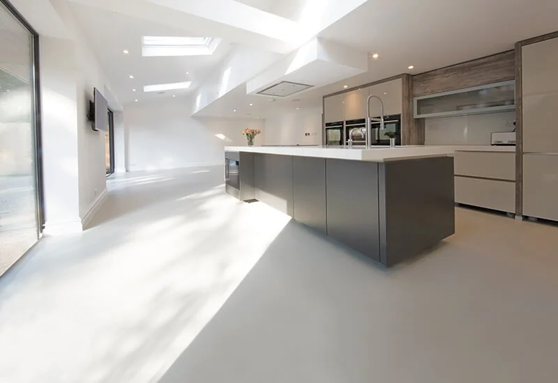 Contemporary kitchen interior highlighting a flawless grey resin floor and a central island unit.