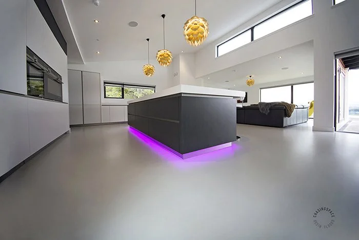 Modern interior featuring an expansive light grey resin floor and a central island with vibrant purple under lighting.