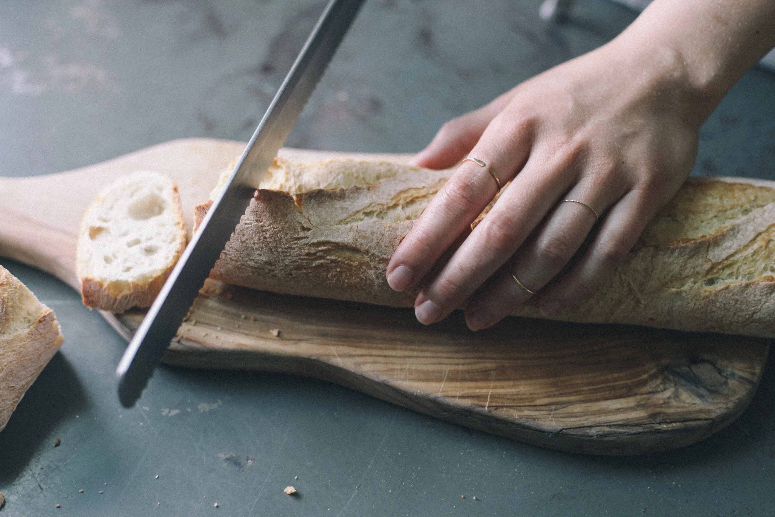 Rebecca is slicing fresh bread to serve with eggs en cocotte. She is wearing Consider The Wldflwr's adjustable stacker , bare gold stacker , and bare gold twist stacker .