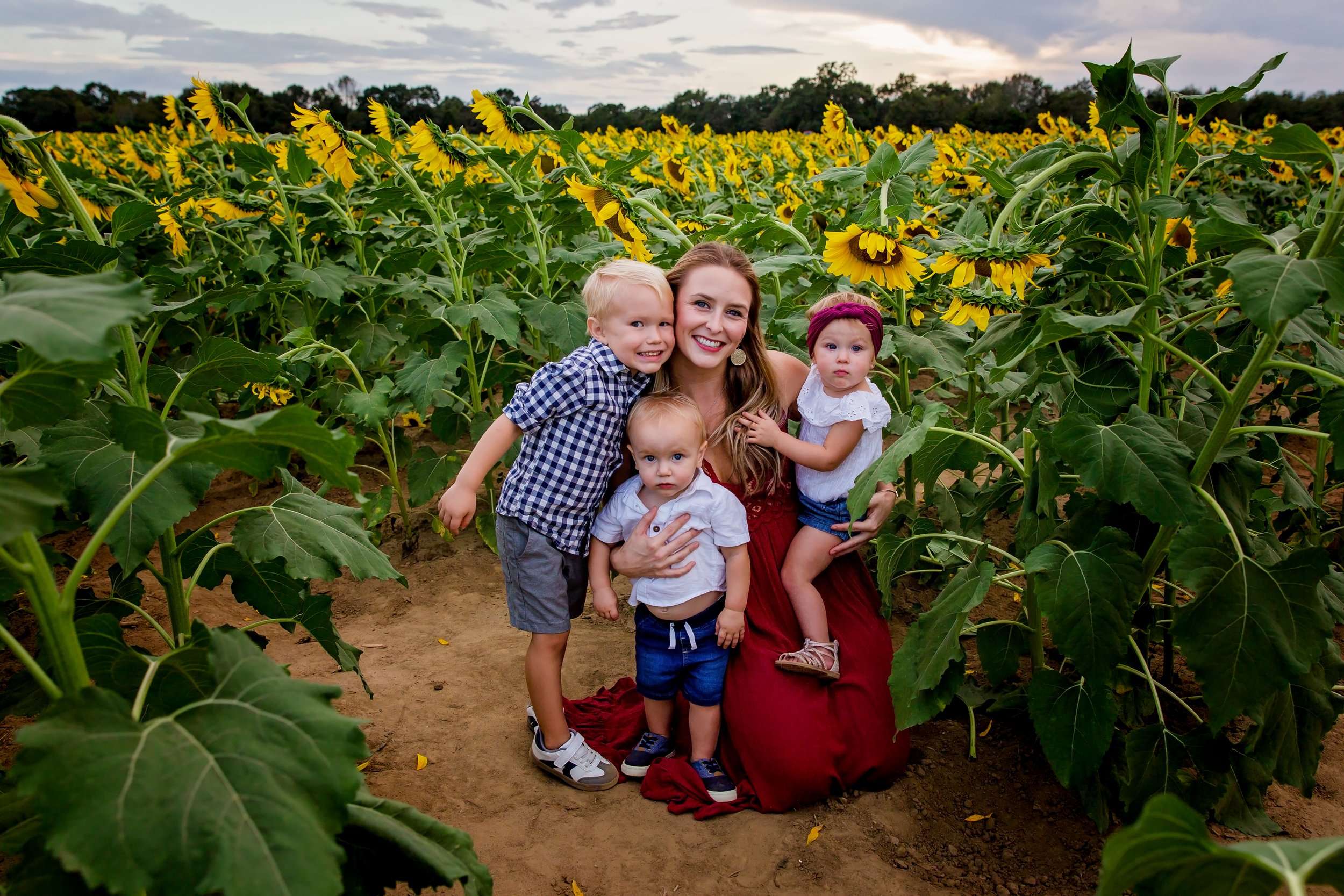 A family portrait holding her children in the middle of a sunflower field in Jacksonville Florida