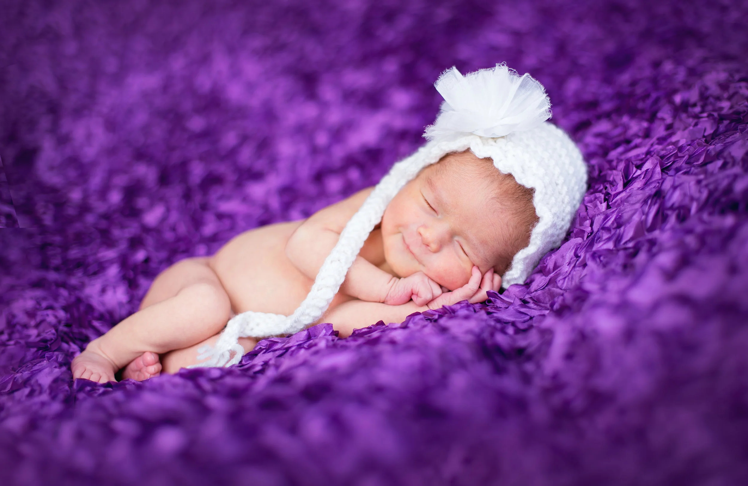 Sleeping newborn baby wrapped in white on a purple blanket during a baby photography session by Inspired By You Photography.