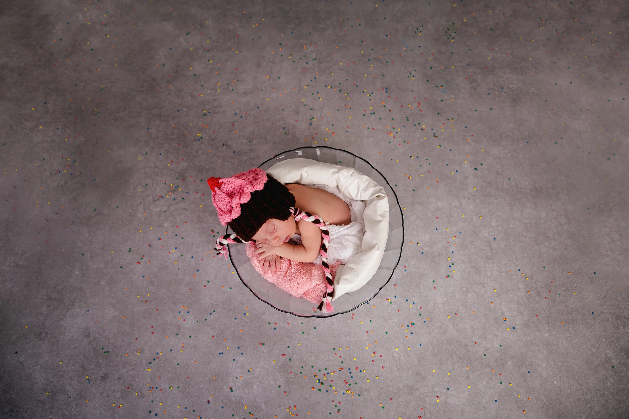 Newborn baby girl sleeping in a small round prop with a pink bow during a professional baby portrait session.