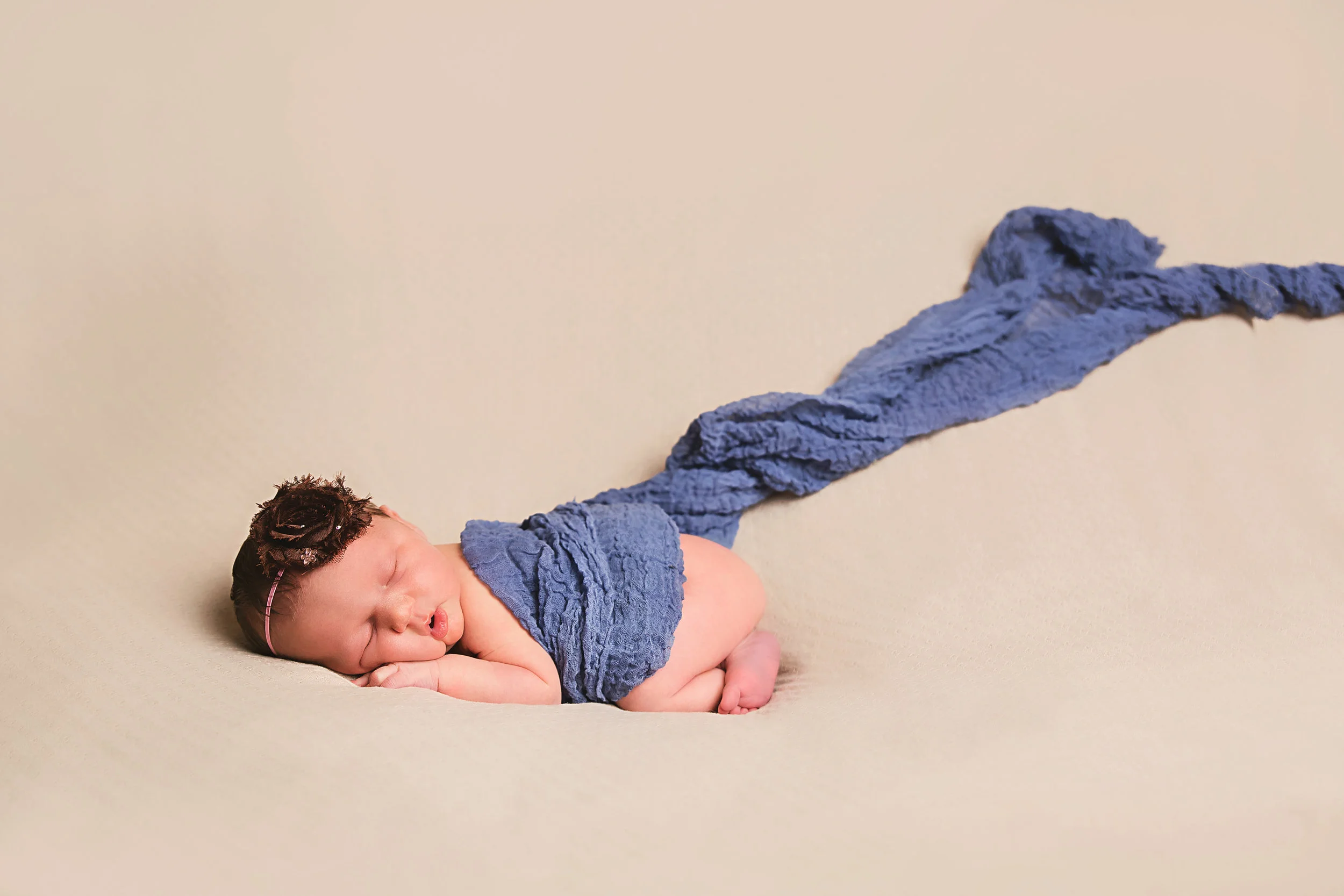 Newborn baby boy sleeping while wrapped in blue during a professional newborn portrait session in Navarre, Florida.
