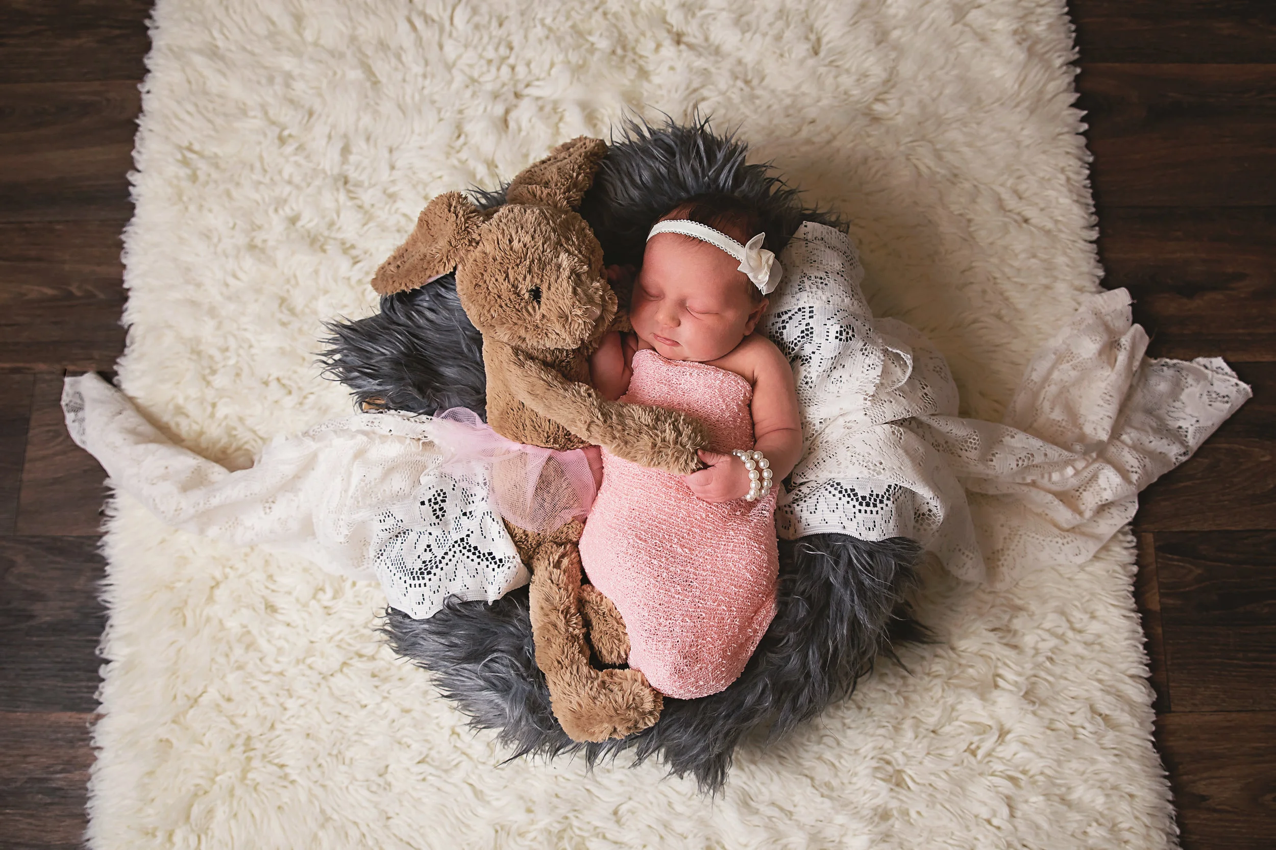 Sleeping newborn baby cuddling a stuffed animal on a soft blanket during a creative baby photography session.