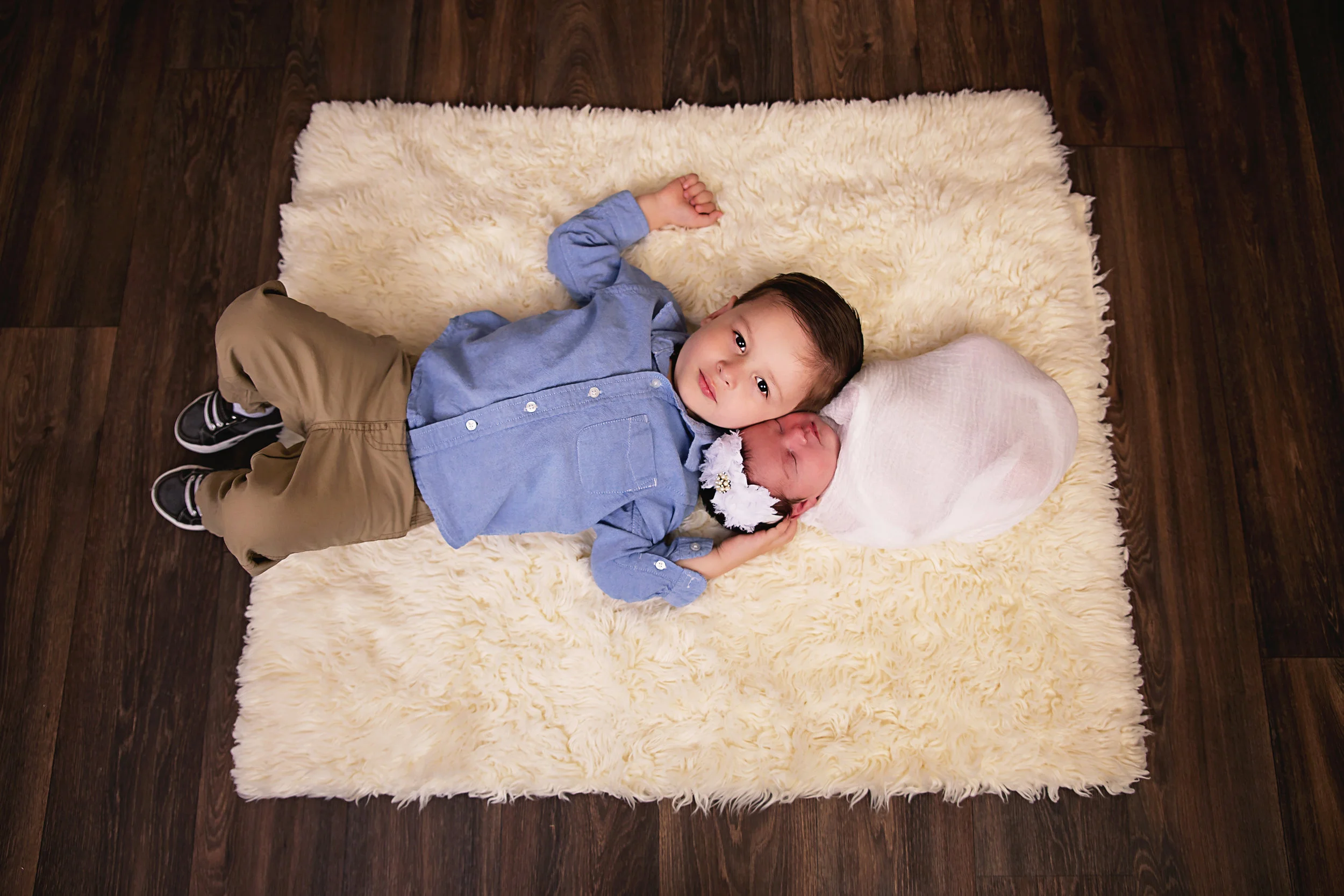 Newborn baby boy dressed in blue and posed on a soft cream rug during a Navarre newborn photography session.